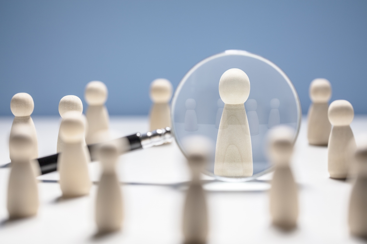 Wooden people with one viewed through a magnifying glass