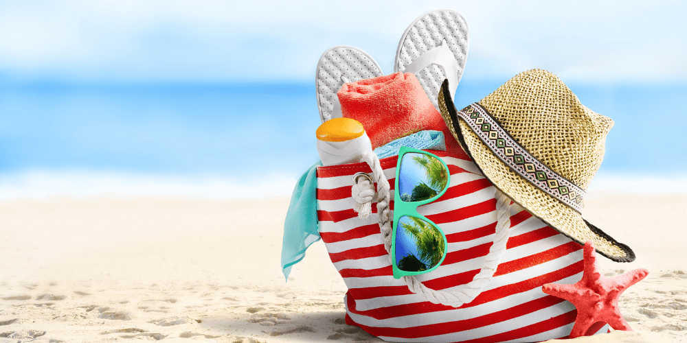 Beach bag on sandy beach filled with holiday essentials.